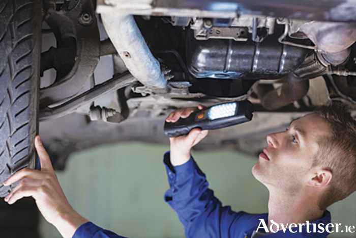 Young mechanic examining car using flashlight