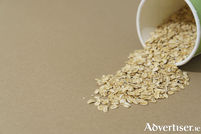 A cardboard paper container spilling dry oatmeal onto a brown paper background with copy space.